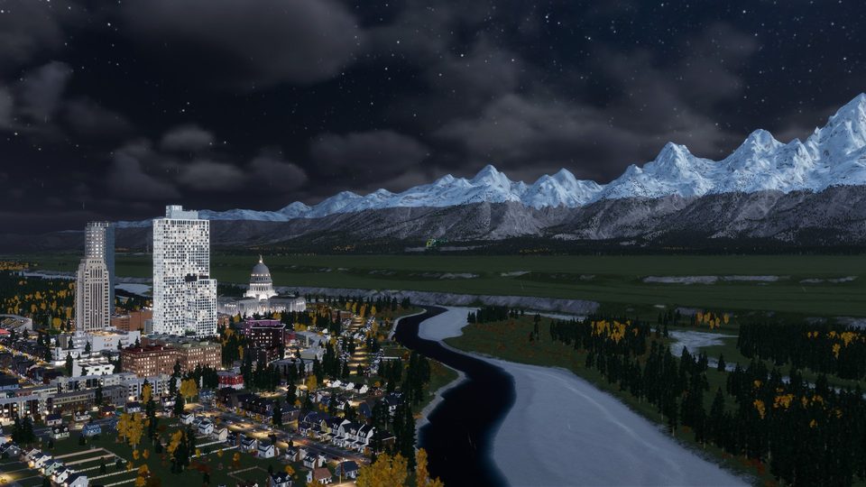 City skyline at night with the capitol building, a river, and snow-capped mountains behind